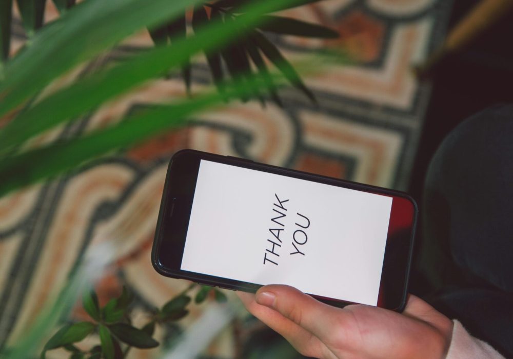 Hand holding smartphone with 'Thank You' message surrounded by lush indoor plants.