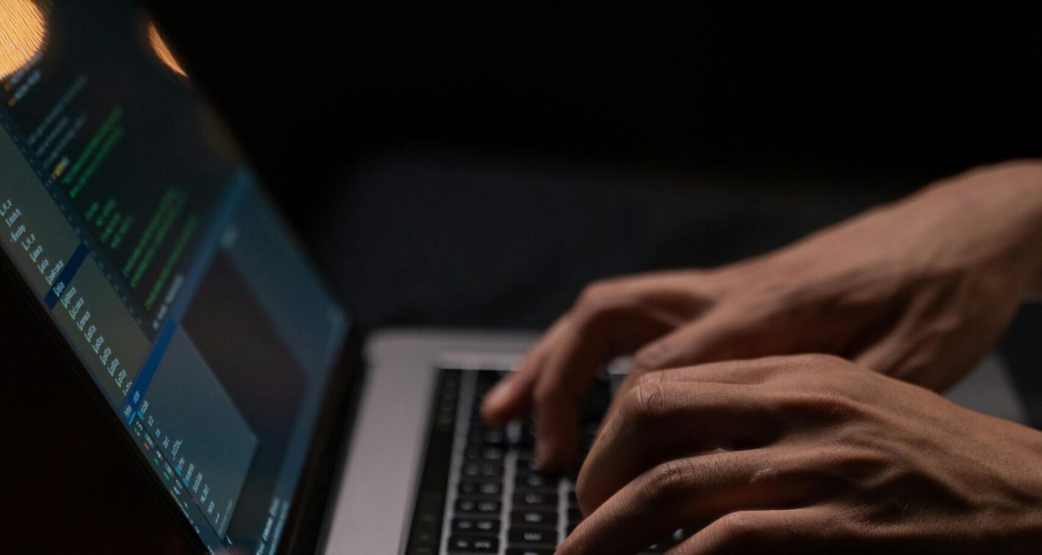 Hands typing code on a laptop keyboard in a dark room, capturing the essence of late-night programming.